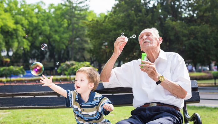 Grandfather blowing bubbles with grandson in a park